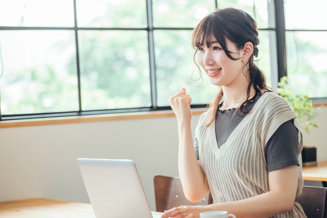 パソコンの前でガッツポーズしている女性の画像